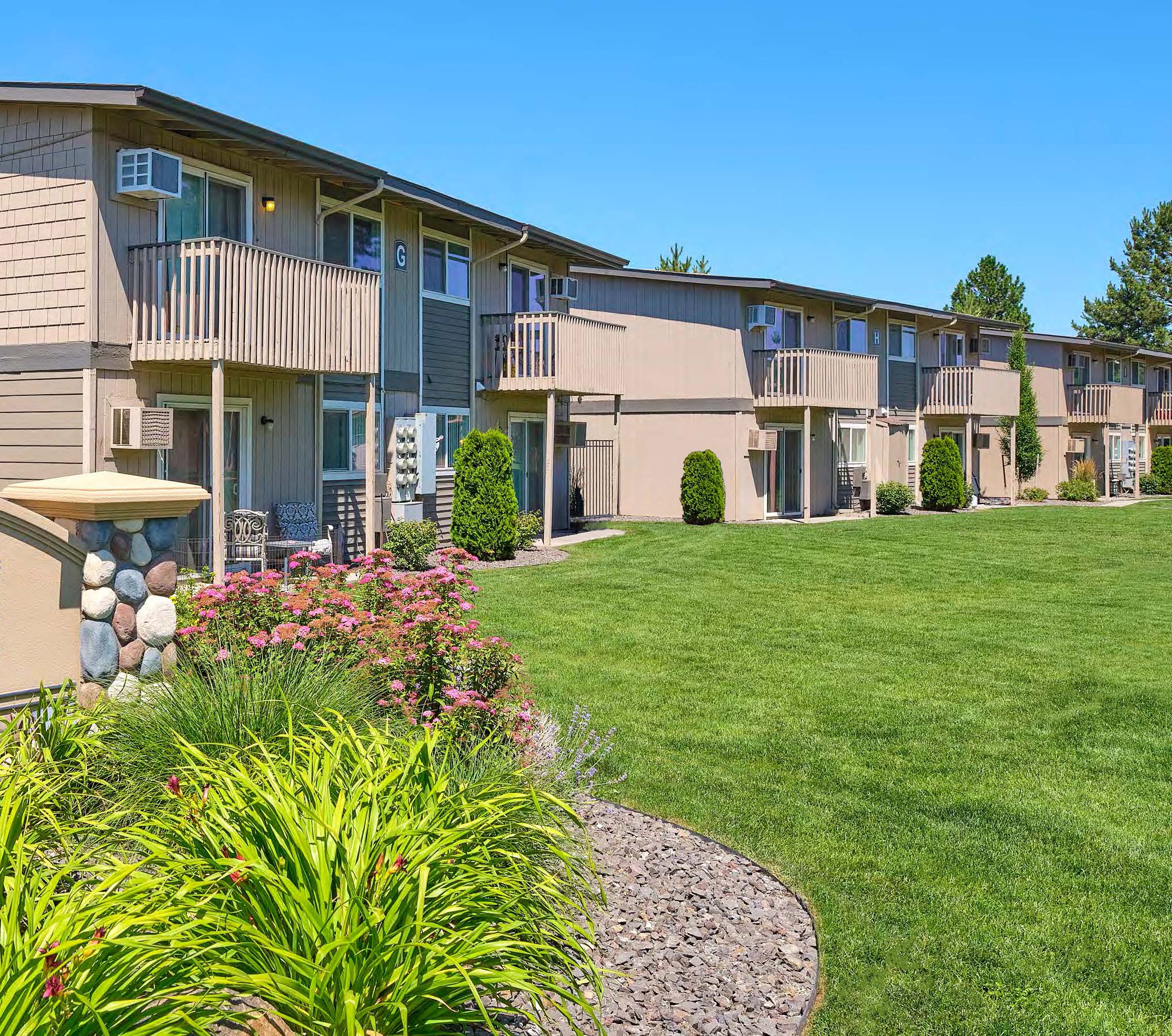 Community exterior with a large grass yard, flower and landscaping with apartments in the background.at Wildflower, Kennewick Washington
